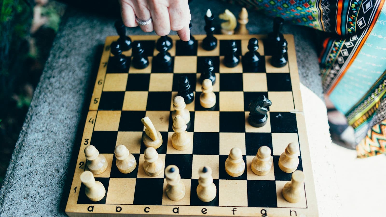 A hand reaching down to move a piece on a wooden chessboard