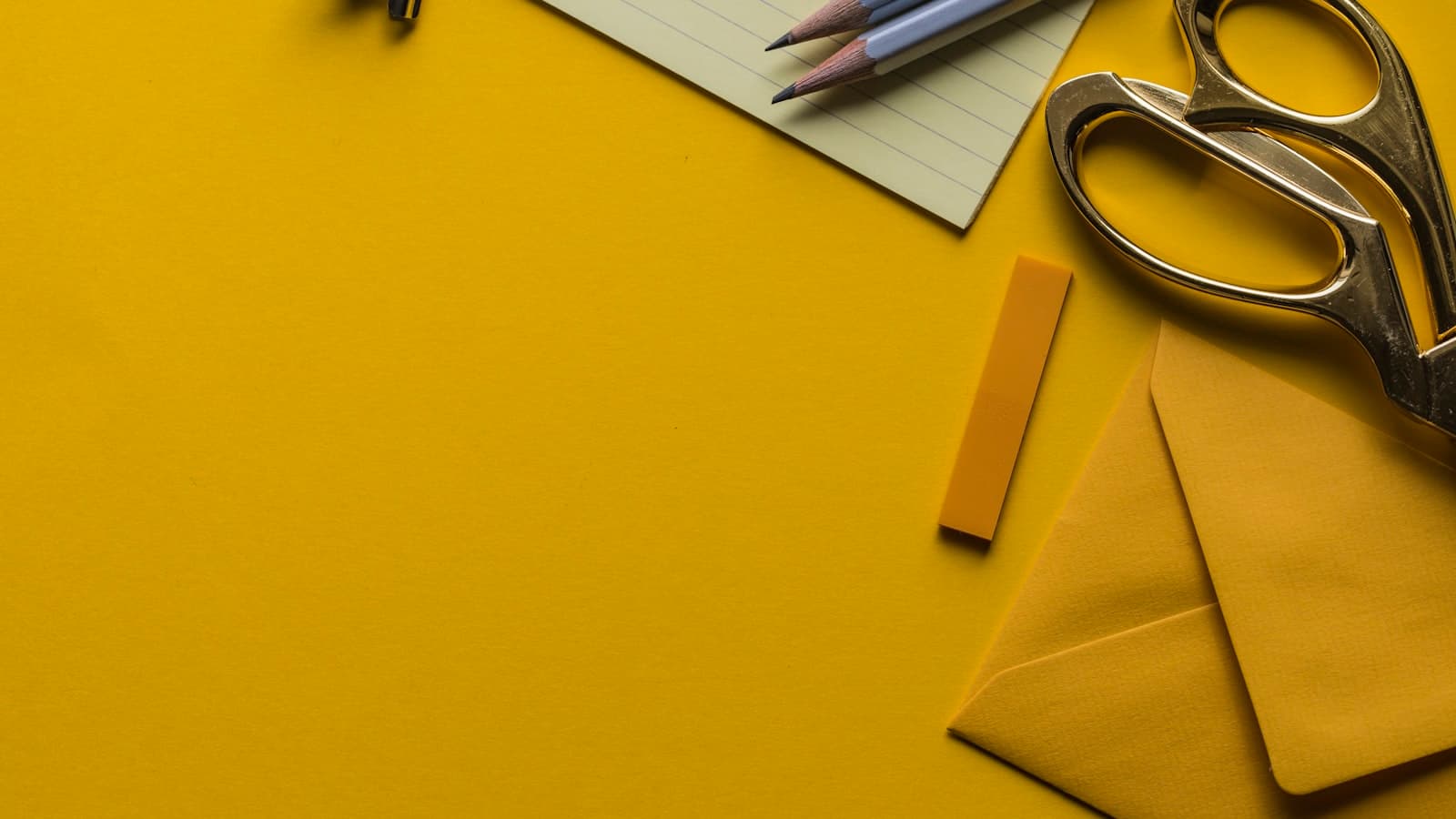 A flat-lay of office supplies — scissors, pencils, and a notepad on a yellow background