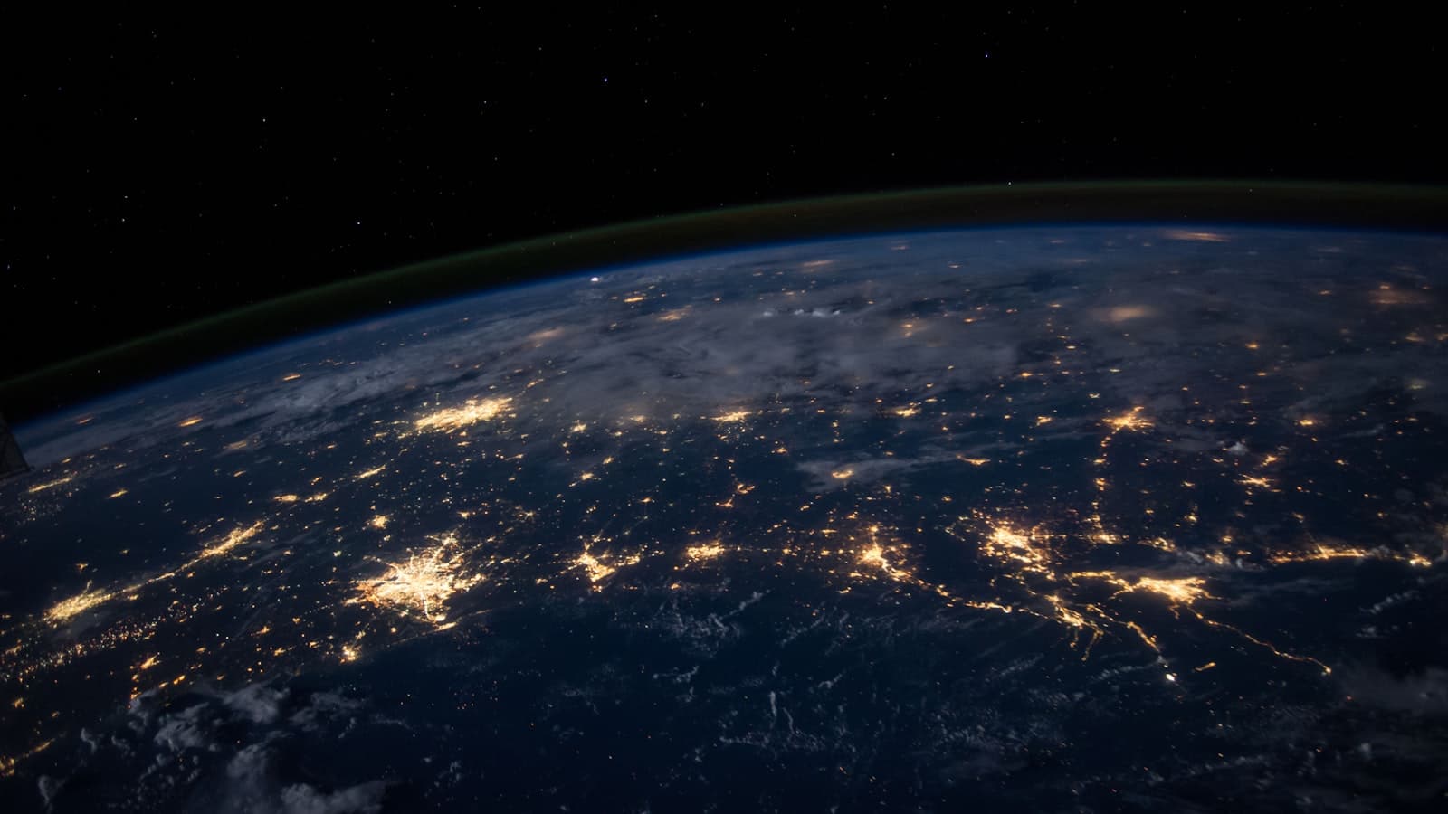 Earth seen from orbit at night, with city lights traced across continents