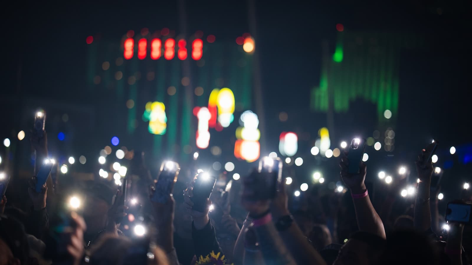A dense crowd at night holding up glowing phone screens toward a stage